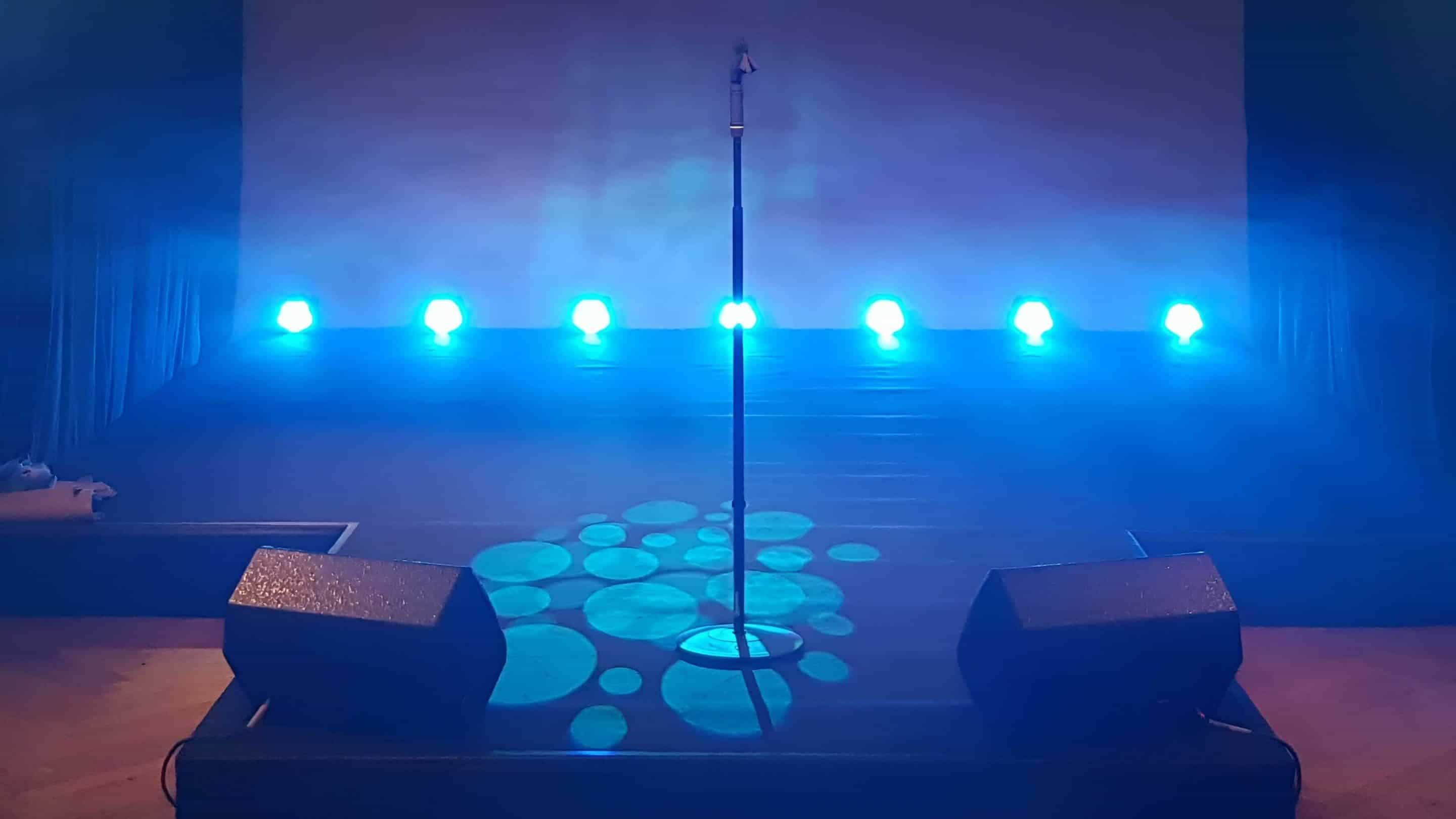 Das Bild zeigt eine Bühne mit Licht, Mikrofon und Lautsprechern und ist ein Bild zur Veranschaulichung der Bühnentechnik